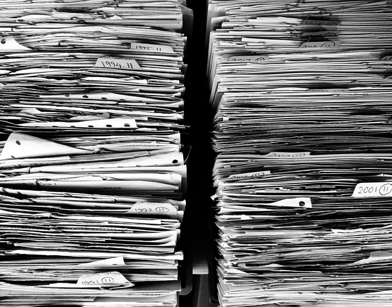 Symbolbild: Hohe Stapel abgehefteter Papierakten in Schwarz-Weiß.