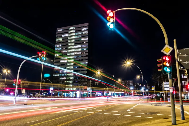 Symbolbild: Ampelgeregelte Straßenkreuzung bei Nacht mit Lichtspuren vorbeifahrender Fahrzeuge.